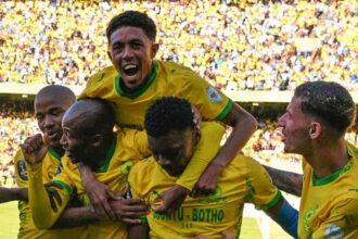Soccer players in yellow jerseys celebrate a goal huddling together as teammates lift one player amid a cheering crowd  trybalnews