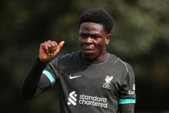 Football player in a dark gray Liverpool training top raising his right hand sweaty and focused on a practice field  trybalnews
