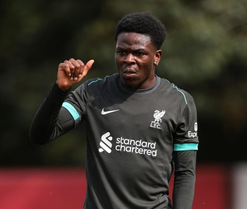 Football player in a dark gray Liverpool training top raising his right hand sweaty and focused on a practice field  trybalnews