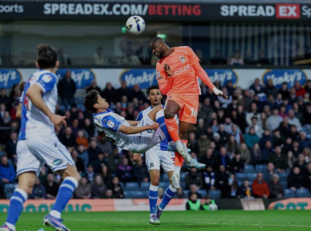 Soccer players contesting a header an orange clad striker leaps while a white blue defender slides in front of him  trybalnews