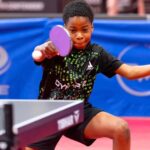 Young table tennis player in a black and green shirt lunges to hit a pink paddle at a ping pong ball focused on the shot on a table tennis table  trybalnews