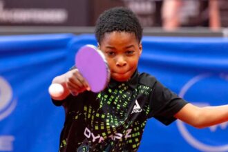 Young table tennis player in a black and green shirt lunges to hit a pink paddle at a ping pong ball focused on the shot on a table tennis table  trybalnews