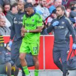 Soccer player in neon green kit 17 walking off the field with two team staff members in dark jackets beside him  trybalnews