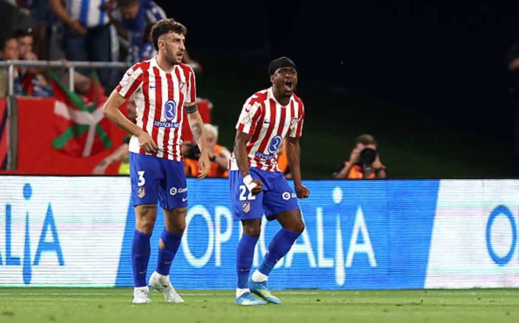Two Atlético Madrid players celebrate on the pitch during a night match with fans in the background  trybalnews
