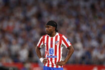 Atlético Madrid footballer wearing the red-and-white striped jersey, hands on hips during a match.