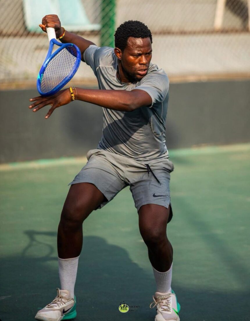 A male tennis player in gray athletic wear swings a blue racket during a match on an outdoor court with a focused expression from the side angle  trybalnews