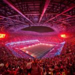 Aerial view of a packed soccer stadium at night with red lighting and a green pitch surrounded by thousands of fans  trybalnews