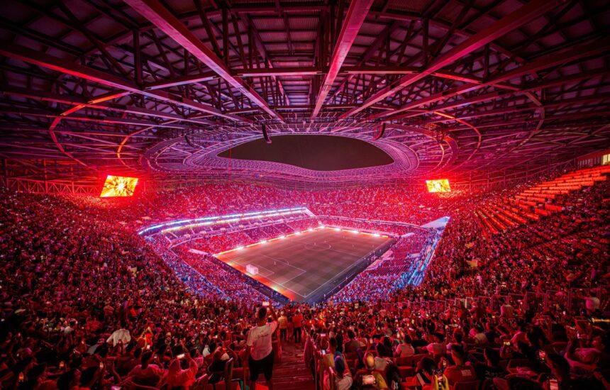 Aerial view of a packed soccer stadium at night with red lighting and a green pitch surrounded by thousands of fans  trybalnews