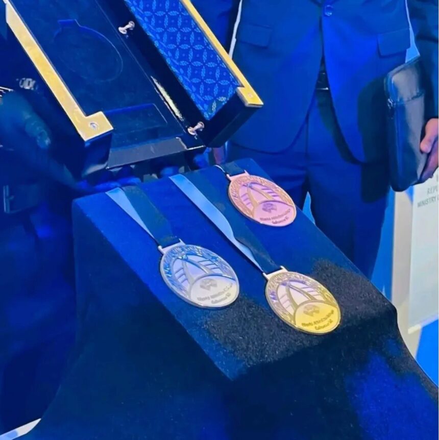 Three circular medals silver bronze gold with blue ribbons laid on a dark blue display cloth a presentation case behind them  trybalnews