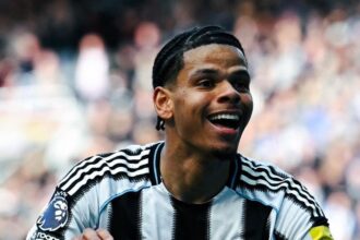 Newcastle United player celebrating with arms outstretched smiling in black and white striped kit on a crowded stadium backdrop  trybalnews