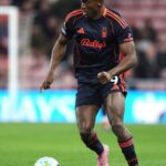 Professional soccer player in a dark navy kit with orange trim dribbling a ball on a grass pitch during a match  trybalnews
