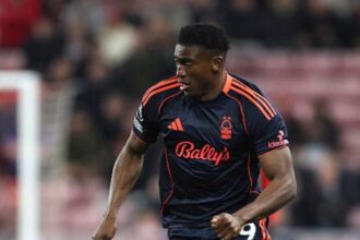 Professional soccer player in a dark navy kit with orange trim dribbling a ball on a grass pitch during a match  trybalnews