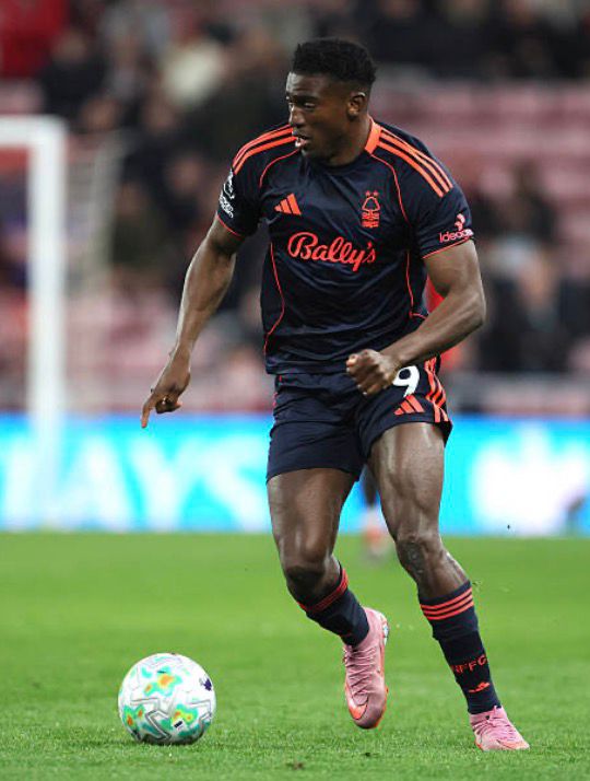Professional soccer player in a dark navy kit with orange trim dribbling a ball on a grass pitch during a match  trybalnews
