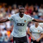 Valencia CF footballer celebrating with arms spread wide and tongue out on the pitch crowd behind him  trybalnews