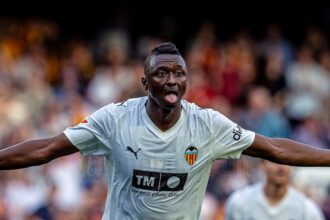 Valencia CF footballer celebrating with arms spread wide and tongue out on the pitch, crowd behind him