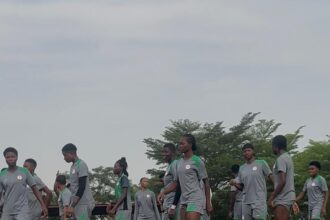 A group of young soccer players in gray uniforms walking in a line on a turf field during practice.