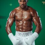 Muscular male boxer in white gloves and shorts fists raised standing in front of a green backdrop  trybalnews