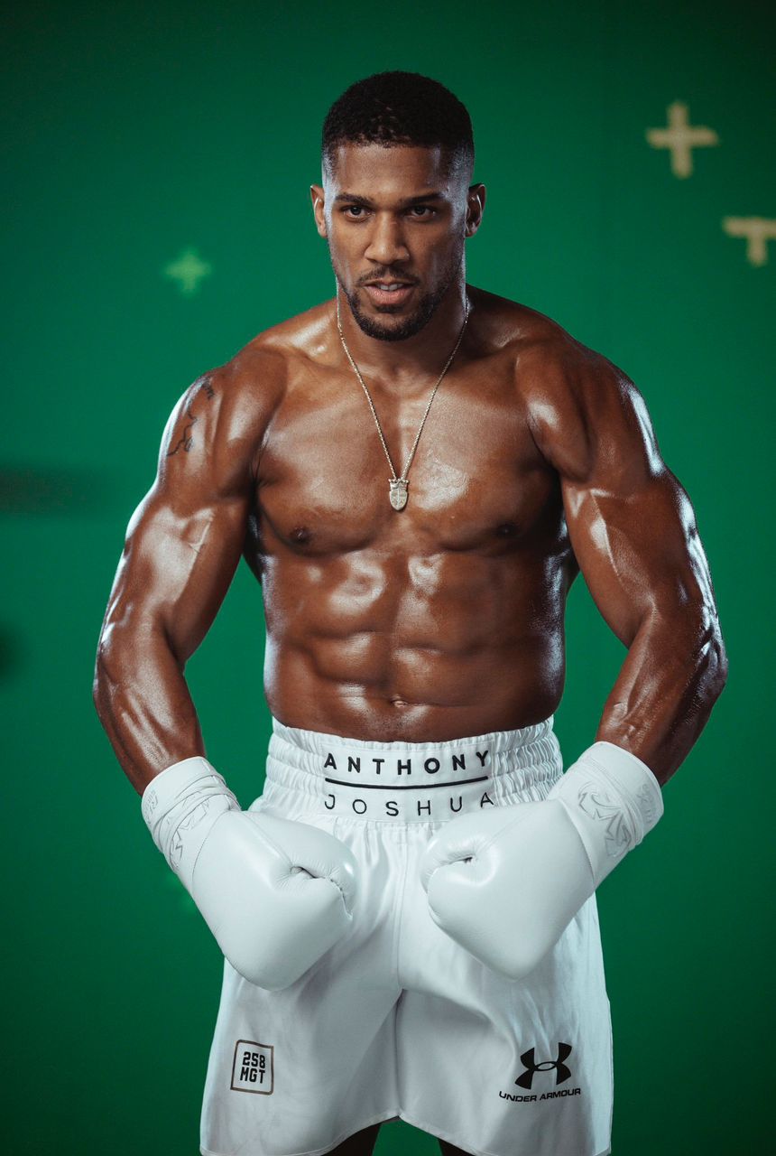 Muscular male boxer in white gloves and shorts fists raised standing in front of a green backdrop  trybalnews