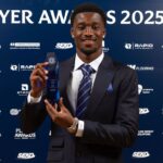 Award recipient in a dark suit and striped tie holding a blue crystal trophy at the Player Awards 202526 backdrop  trybalnews