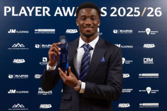 Award recipient in a dark suit and striped tie holding a blue crystal trophy at the Player Awards 2025/26 backdrop