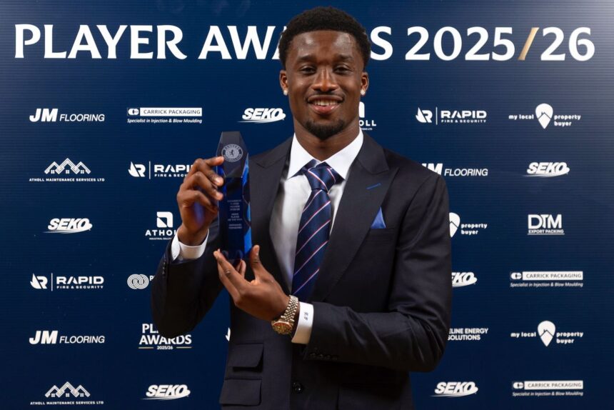 Award recipient in a dark suit and striped tie holding a blue crystal trophy at the Player Awards 202526 backdrop  trybalnews