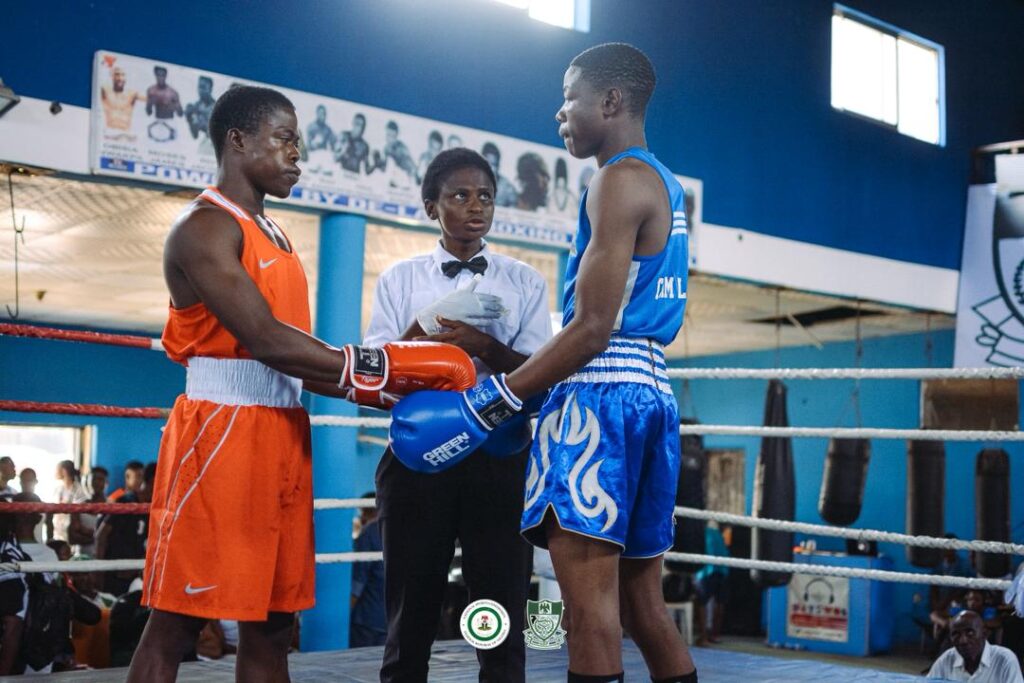 WhatsApp Image 20260429 at 104643 Trybal News Two young boxers in orange and blue trunks shake hands in the ring as a referee looks on in a gym boxing match area trybalnews