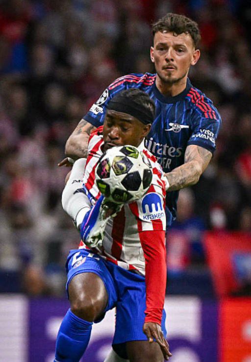 Two soccer players battle for the ball during a match one in a red and white striped jersey and blue shorts the other in a dark blue kit in close pursuit  trybalnews