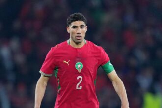 Moroccan national team footballer in red jersey with number 2 on the front, standing on the field.