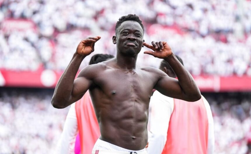 Athlete in a stadium celebration shirtless with hands raised near his ears as the crowd cheers behind him  trybalnews