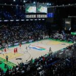 Packed basketball arena during a live game players on court sponsor banners along the sidelines  trybalnews