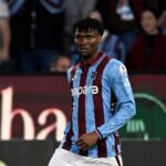 Professional footballer in blue and maroon striped jersey running on a soccer field with spectators in the stands behind him  trybalnews
