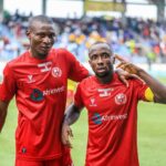 Two male soccer players in red uniforms pose with their arms around each other on a grassy field stadium crowd in the background  trybalnews