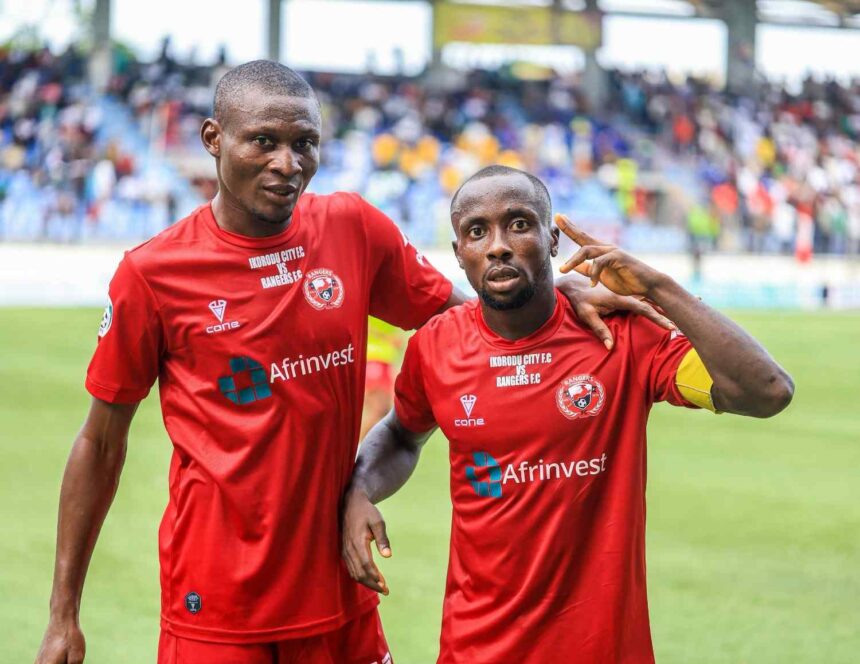 Two male soccer players in red uniforms pose with their arms around each other on a grassy field stadium crowd in the background  trybalnews