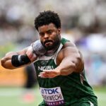 Nigerian male shot put athlete in green uniform throwing a shot put during a competition with a blurred stadium crowd in the background  trybalnews