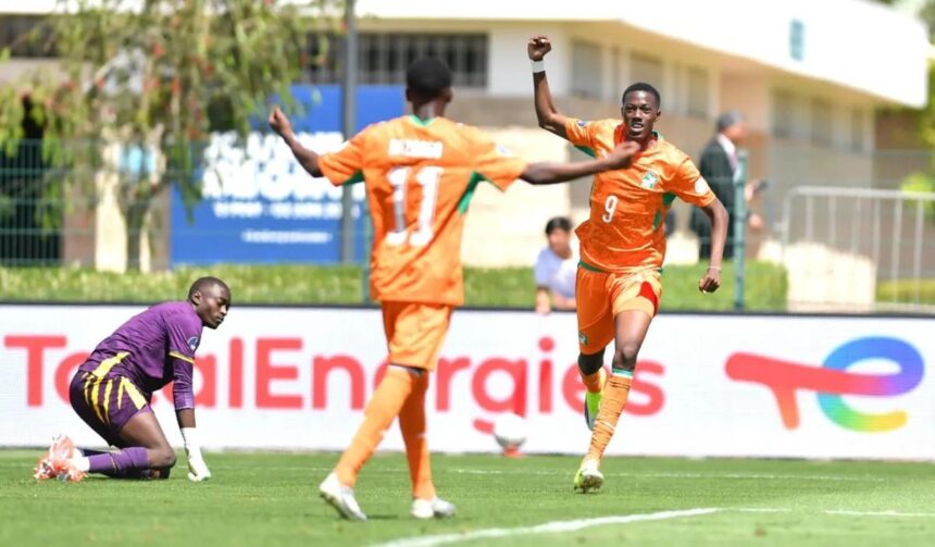 Orange clad soccer players celebrate a goal as one raises a fist while a teammate approaches a purple clad goalkeeper kneels on the turf nearby  trybalnews