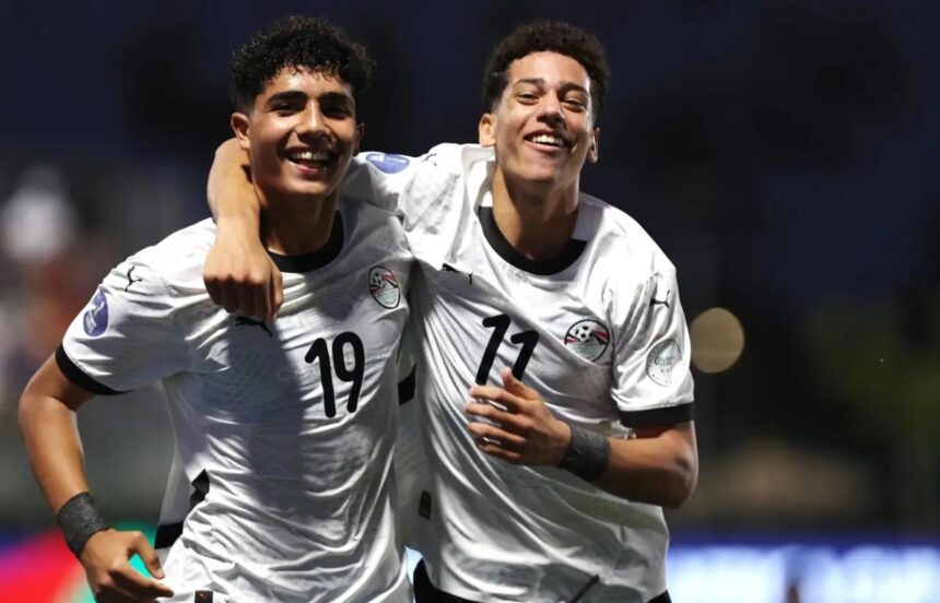 Two soccer players in white jerseys celebrate with their arms around each other on the field smiling broadly  trybalnews