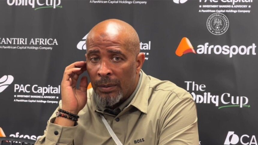 Eric Chelle in a beige shirt sits at a press backdrop touching his ear with his left hand during a post match interview  trybalnews