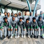 Team of young athletes in gray and green tracksuits posing for a group photo outdoors in front of a modern building with blue arches outside  trybalnews