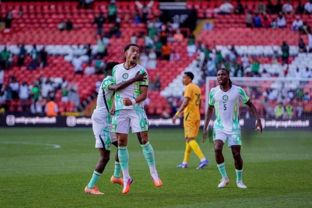 Two Nigerian players in white green kits celebrate a goal on the pitch as a teammate joins them in the hug with more players and a yellow clad opponent in the background  trybalnews