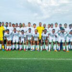 Wide group of young soccer players posing on a green field in white kits with green trim plus yellow jersey goalkeepers under a cloudy sky  trybalnews
