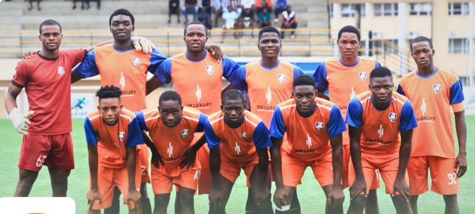 G12FC Trybal News A group of ten male soccer players posing for a team photo on a green field wearing orange training kits with blue sleeves and a logo on the chest trybalnews