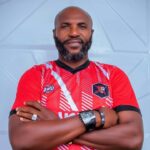 Man with a beard wearing a red sports jersey arms crossed standing against a light blue wall  trybalnews