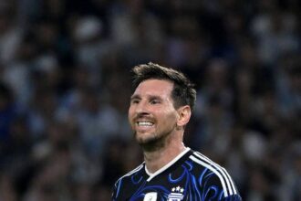 Soccer player in an Argentina blue-black jersey, with captain's armband, smiling on the field.