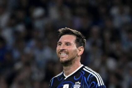 Soccer player in an Argentina blue-black jersey, with captain's armband, smiling on the field.