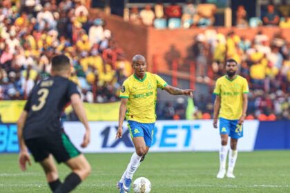 Soccer player in a yellow jersey controls the ball on the green field while a crowd watches from the stands.
