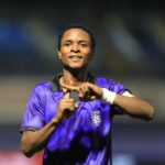 Soccer player in a purple jersey on a stadium field smiling and making a hand gesture with both hands to celebrate the moment  trybalnews