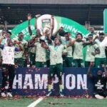 Soccer team and fans celebrate on the pitch holding a CHAMPION banner as confetti falls  trybalnews