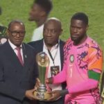 Group of men on a soccer field presenting a trophy to a player in a bright pink jerseykit  trybalnews