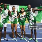Four Nigerian athletes on a track celebrate a win holding a green and white flag behind them wearing Team Nigeria uniforms with bib numbers 483 506 665 and 475  trybalnews