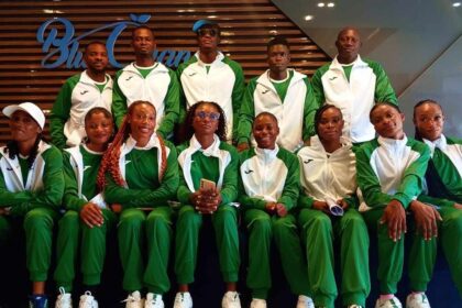 Group of athletes in matching green and white tracksuits posing for a team photo indoors.